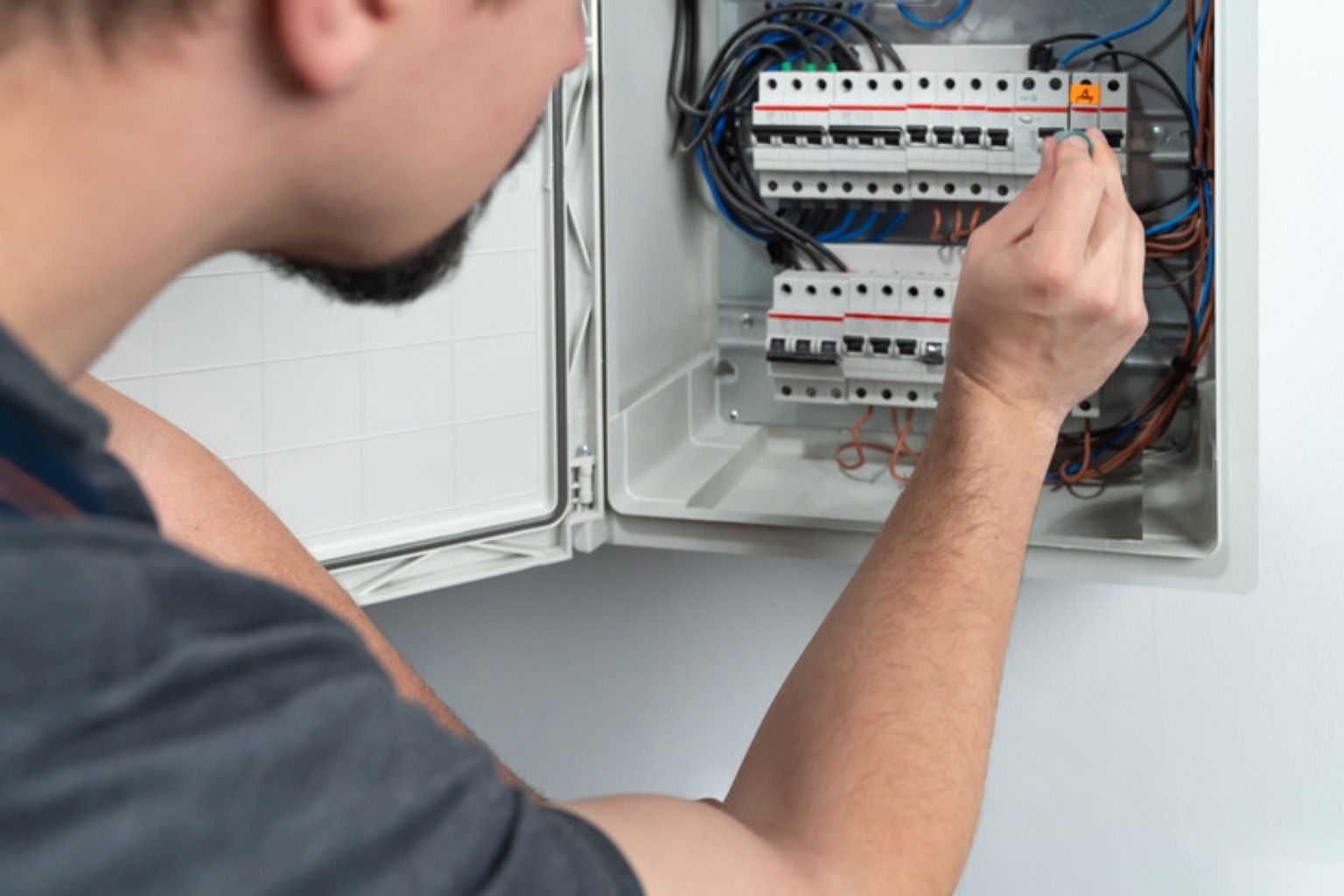 Elektriker arbejder på automatsikringer i en åben eltavle på en hvid væg